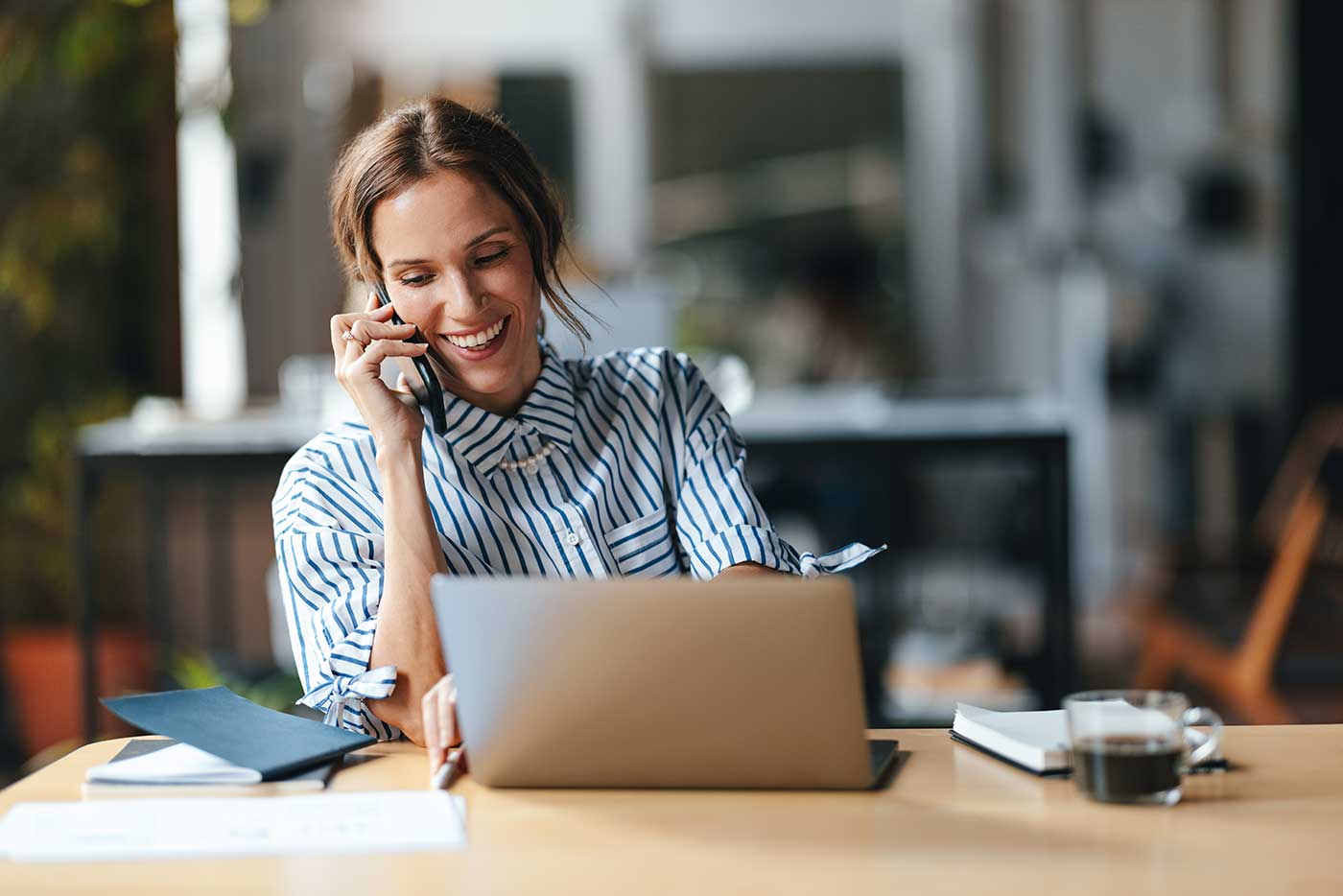 Frau mit Phone am Ohr vor Laptop.