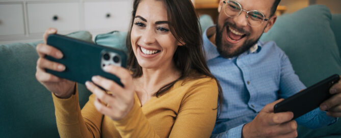 Aufnahme eines jungen Paares, das zu Hause im Wohnzimmer faulenzt und mit dem Handy Spiele spielt.