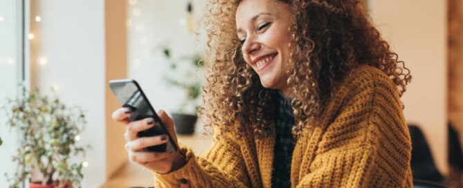 Lächelnde Frau, die im Café auf ihrem Handy schreibt.