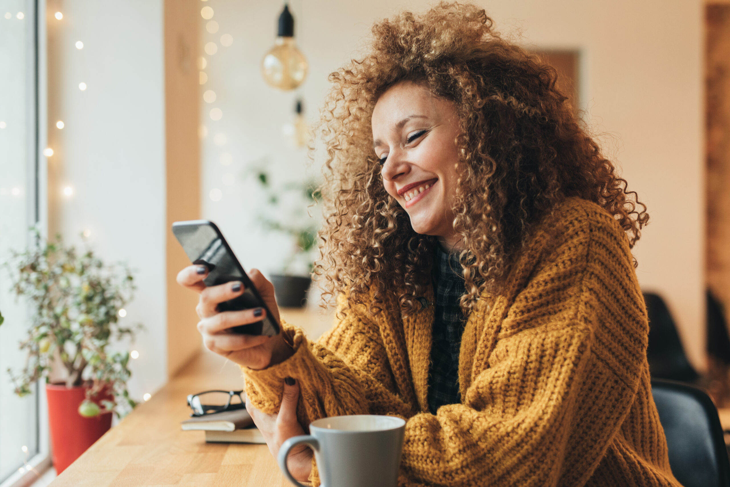 Smiling woman writing on her cell phone in a café.