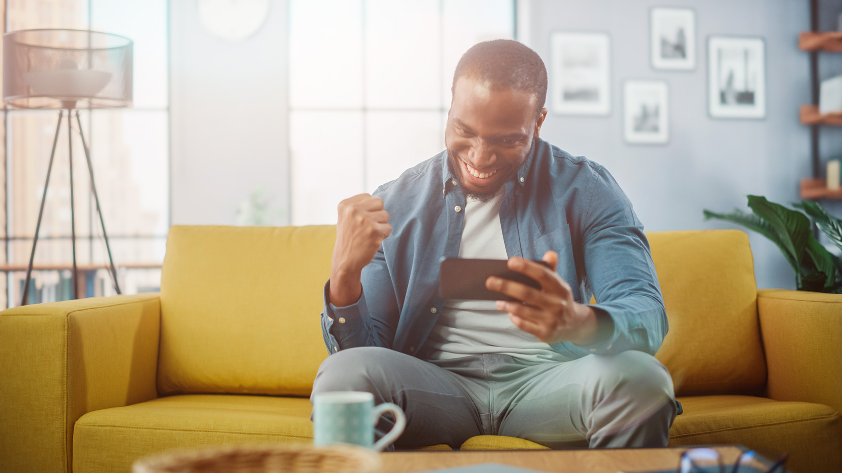Someone is sitting on a sofa, looking at their cell phone and is happy about something he sees there.