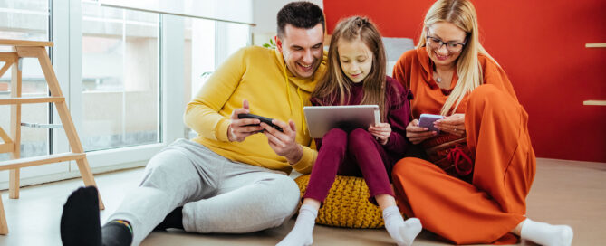 Mutter, Vater und Kind sitzen auf einem Sitzsack. Jeder hat ein Mobile-Gerät in der Hand und spielt darauf rum.
