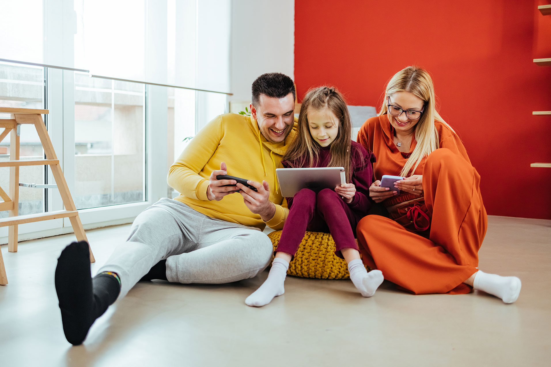 Mutter, Vater und Kind sitzen auf einem Sitzsack. Jeder hat ein Mobile-Gerät in der Hand und spielt darauf rum.