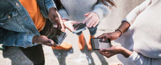 Eine multiethnische Gruppe von Freunden tauscht über ihre verschiedenen Mobilgeräte Inhalte aus sozialen Medien miteinander aus. Blick von oben auf die Smartphones.