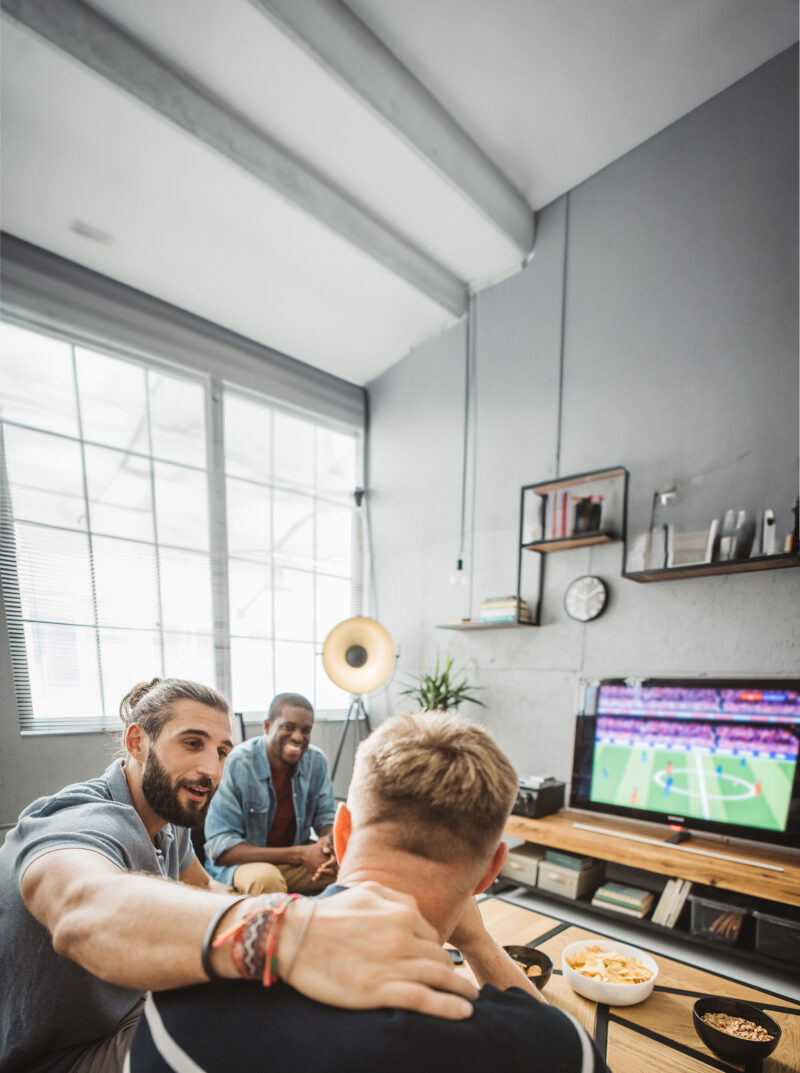 Eine bunte Gruppe von Männern, die zu Hause ein Fussballspiel anschauen und ihre Lieblingsmannschaft anfeuern.
