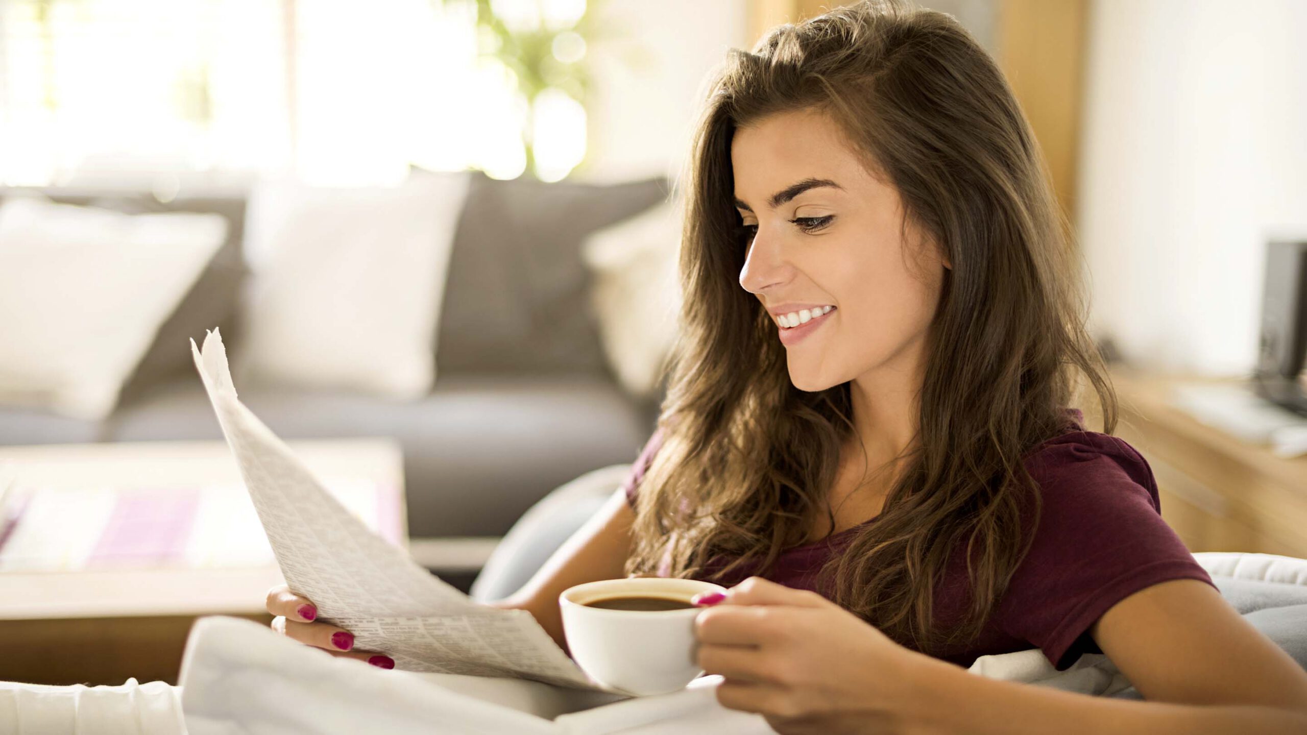 Woman sitting in a café drinking coffee and reading a newspaper