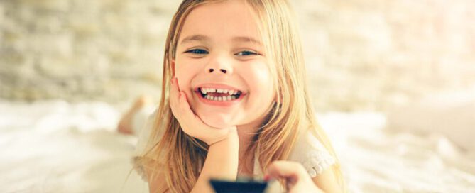 Child lying happily on the bed with a remote control in hand and watching TV.