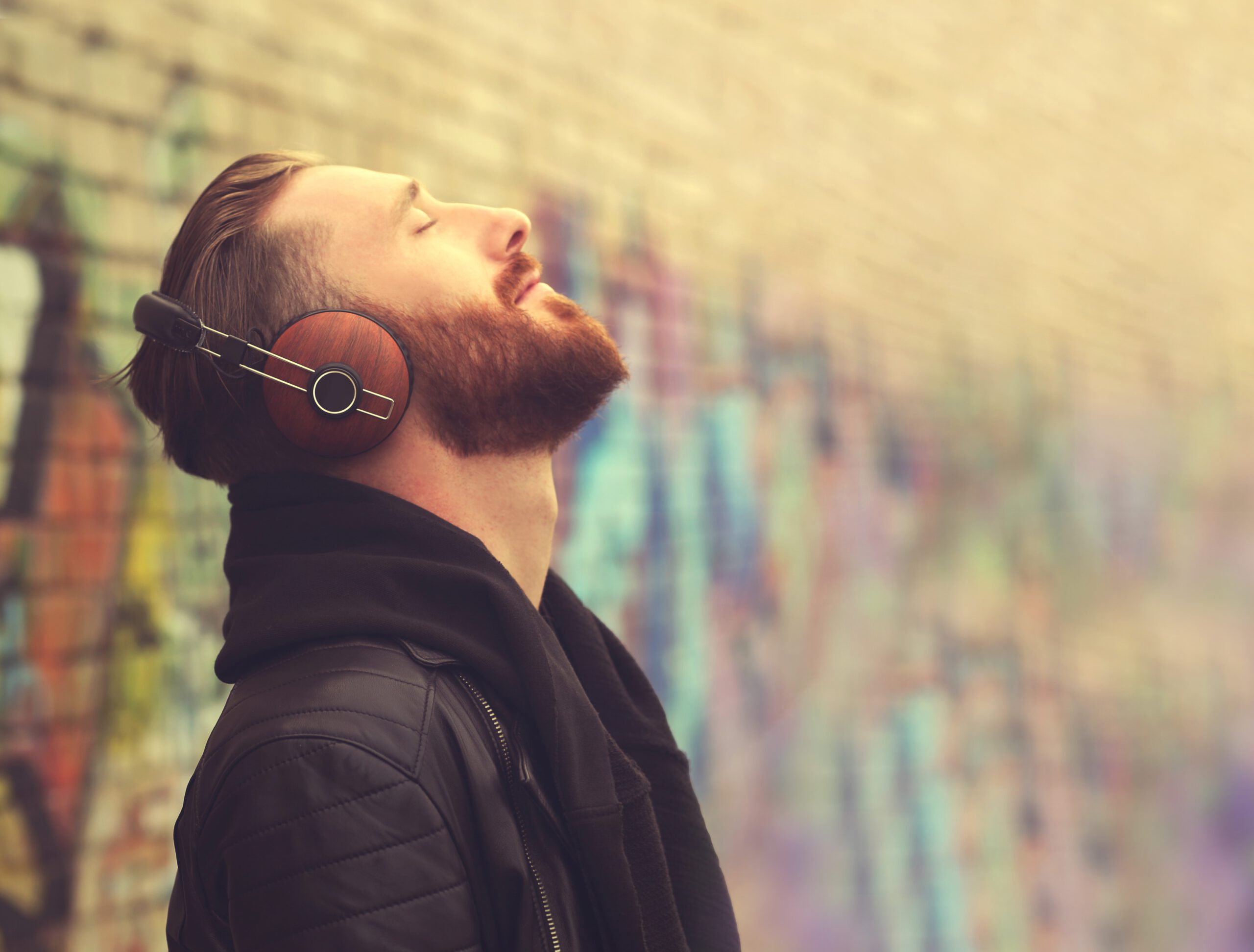 Mann mit Kopfhörern steht an Wand mit Graffiti und hört Audio