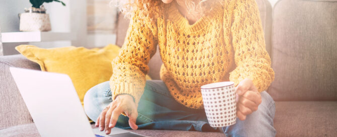 Une femme avec une tasse de café assise sur un canapé et regardant un ordinateur portable