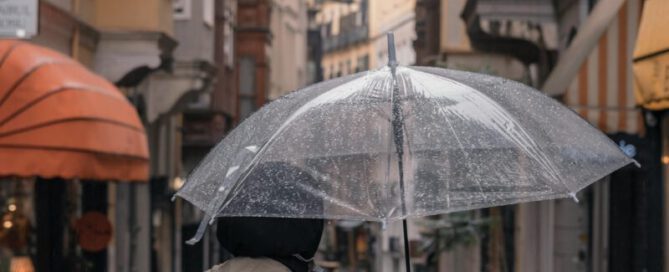 Frau steht mit Schirm in einer kleinen Stadt bei Regen