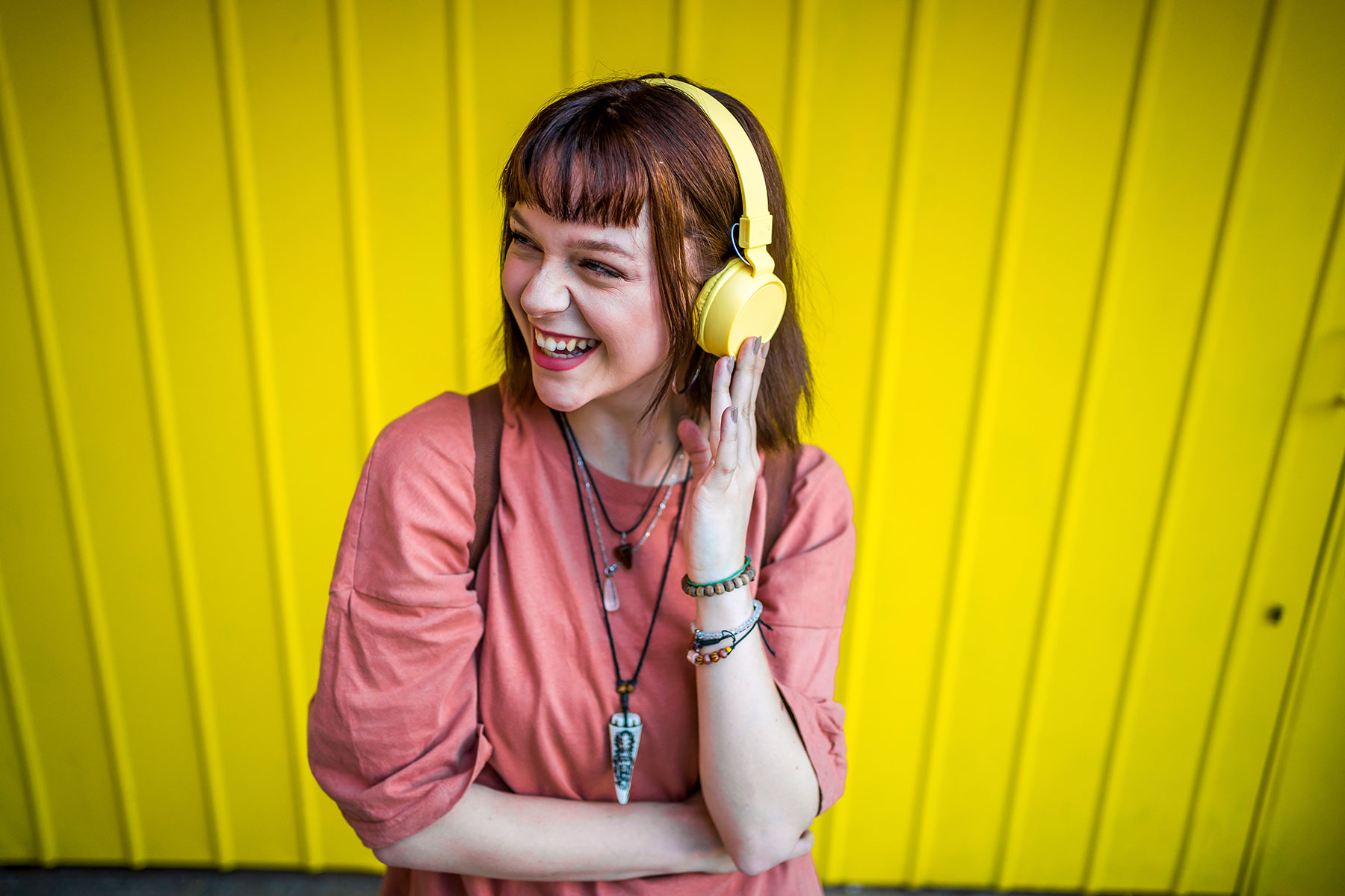 Junge Frau hört Musik mit Kopfhörern vor knallgelber Wand.