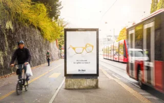 OOH-Plakat an der Kornhausstrasse in Bern mit Menschen im Vordergrund und einer vorbeifahrenden Tram.