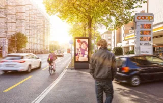 Advertising screen next to a petrol station with a car driving into the station and a person walking past