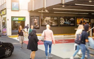 Multiple posters at garage entrance with people walking past