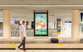 Advertising space and person waiting for luggage at baggage carousel