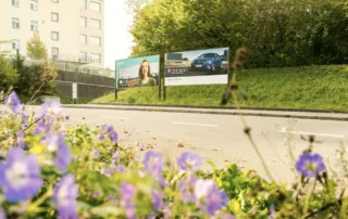 Two advertising spaces at the side of the road and people walking past. 